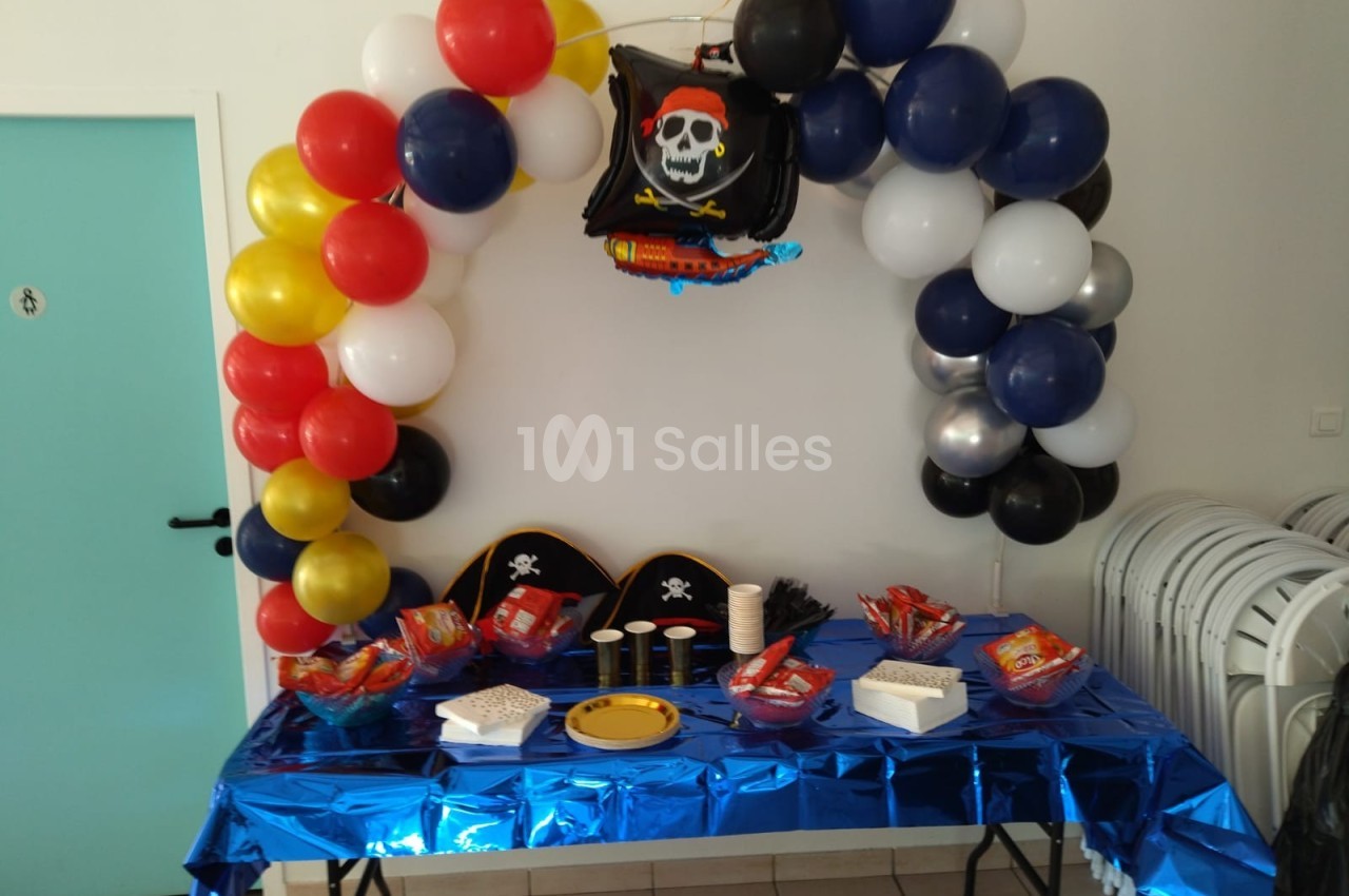 Décoration de fête sur le thème des pirates avec ballons colorés, chapeaux, snacks et nappe bleue sur une table.