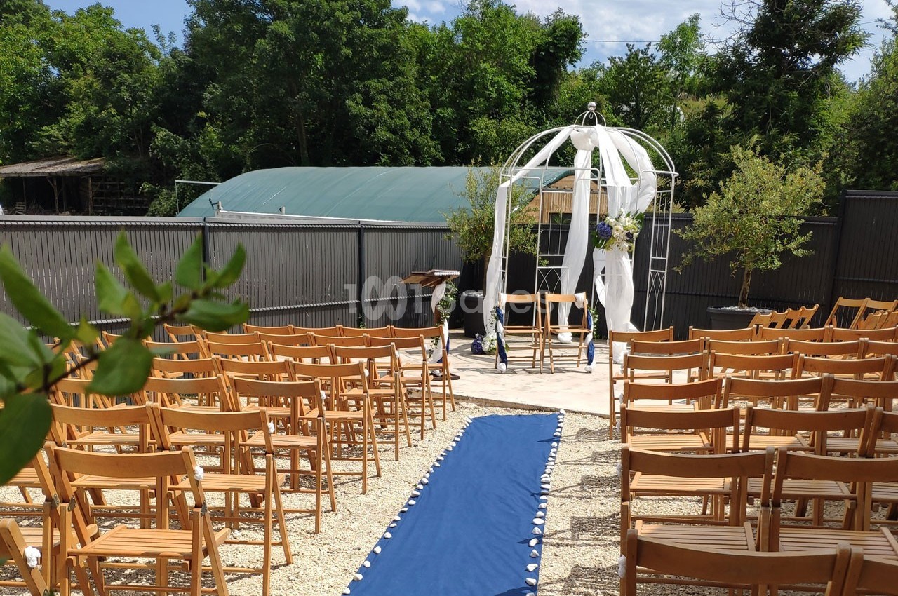 Allée centrale bordée de chaises en bois menant à une arche décorée pour une cérémonie en extérieur.