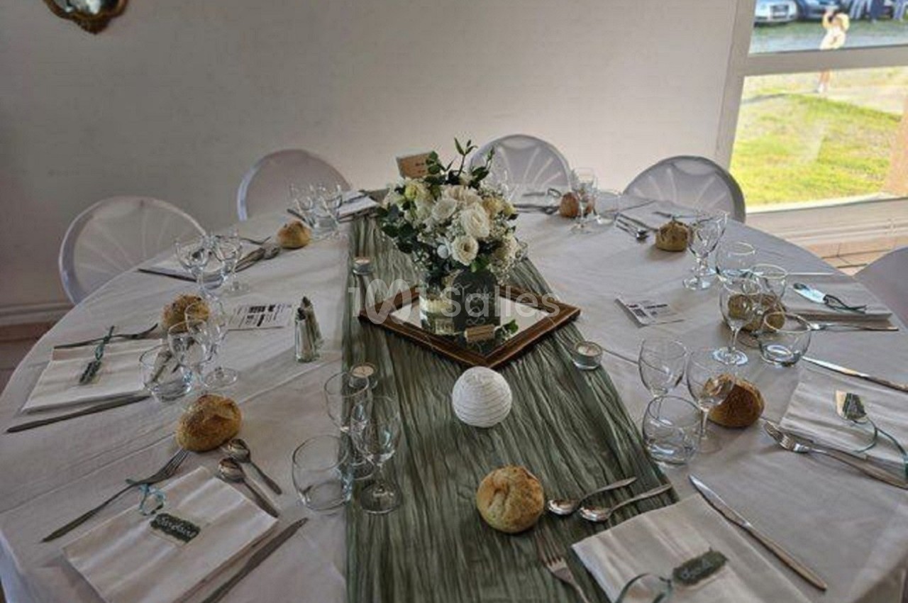 Table ronde dressée pour un repas, décorée avec une nappe blanche, un chemin de table vert et un centre floral.