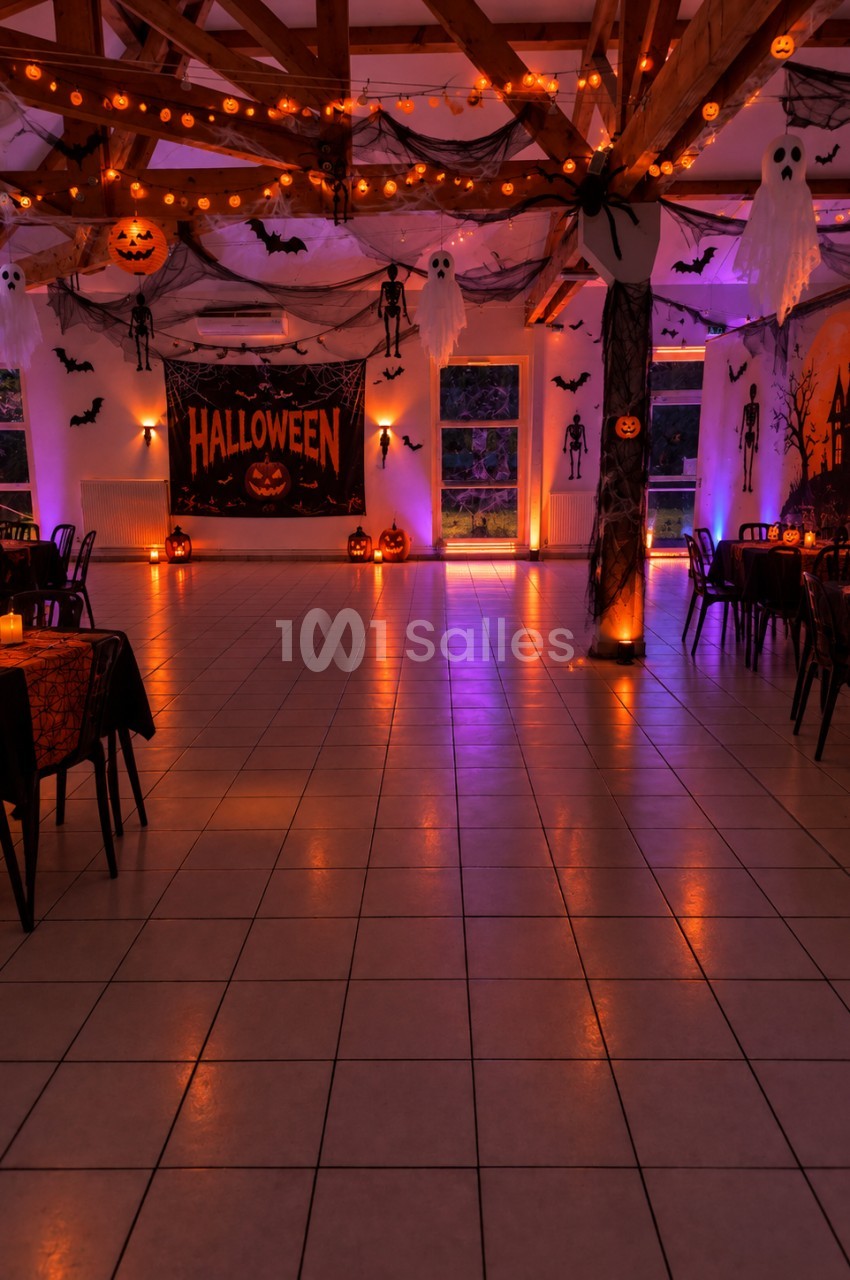 Salle décorée pour Halloween avec guirlandes lumineuses, citrouilles, fantômes suspendus et affiches thématiques.