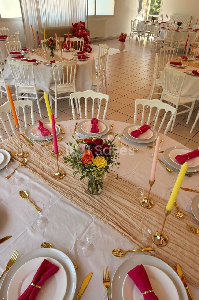 Salle de réception décorée avec des tables dressées, nappes blanches, bougies colorées et compositions florales.