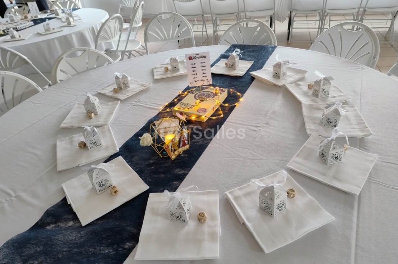 Table décorée avec des nappes blanches, lanternes dorées, bougies et petits cadeaux sur des serviettes pliées.
