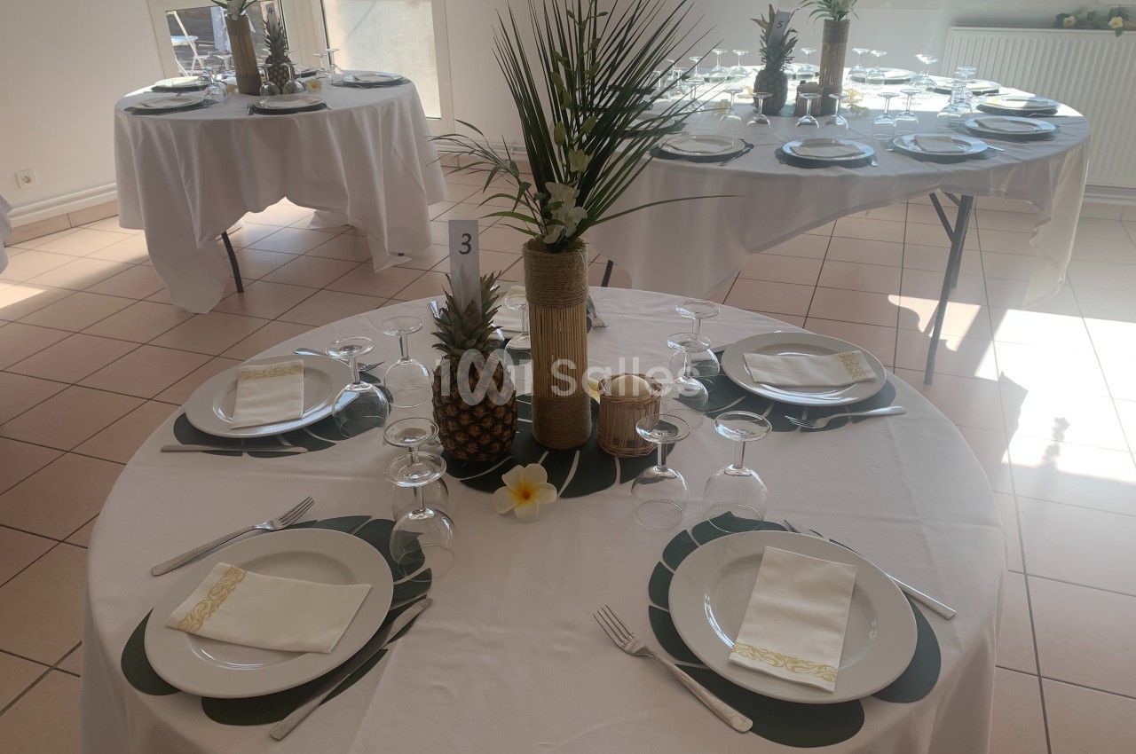 Table dressée avec une décoration tropicale, comprenant des ananas, des feuilles et des fleurs, dans une salle lumineuse.