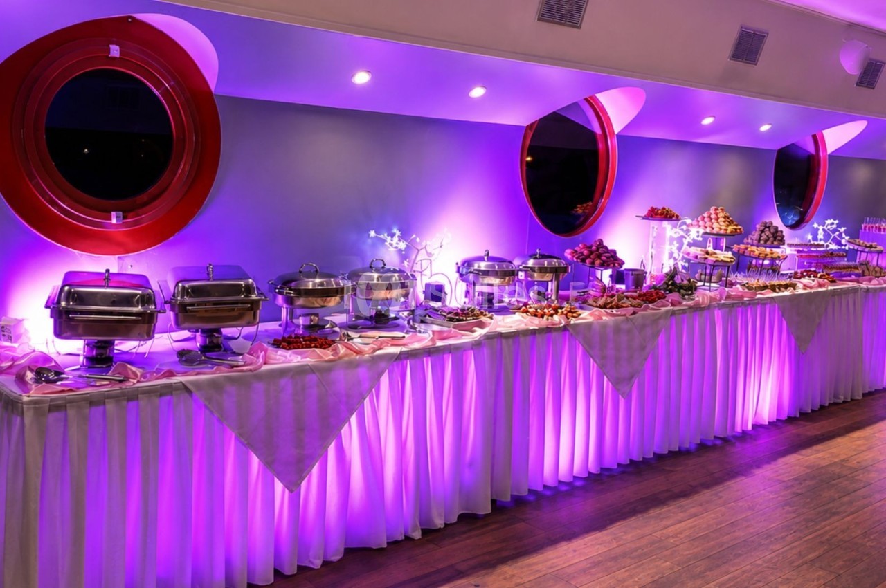 Buffet varié avec plats chauds et froids disposés sur une longue table éclairée par une lumière violette.