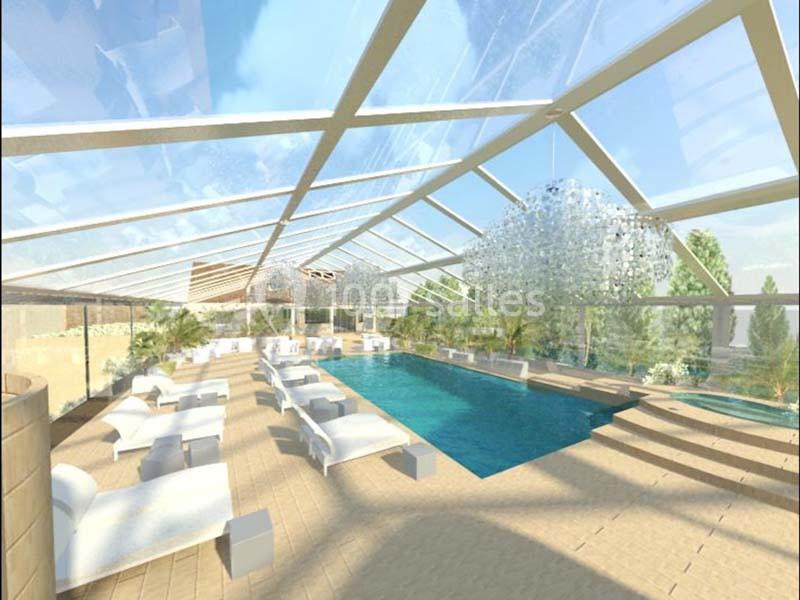 Piscine intérieure lumineuse avec toit en verre, entourée de chaises longues et de végétation.
