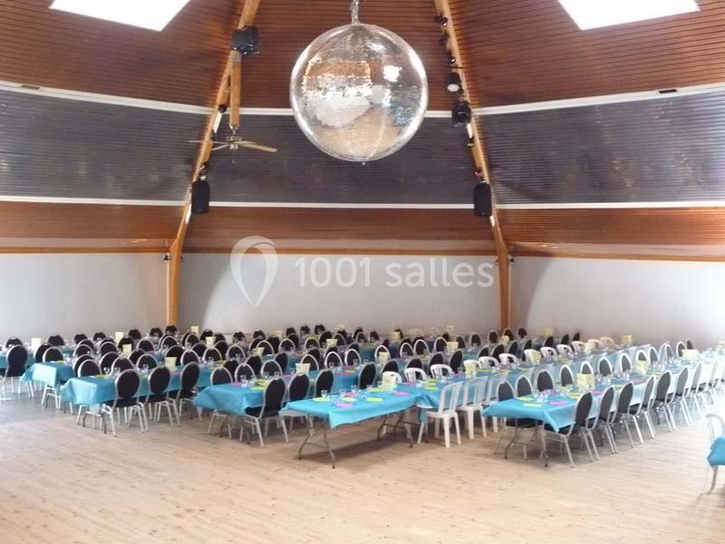 Salle de réception avec tables rectangulaires dressées de nappes bleues et une grande boule disco suspendue au plafond.