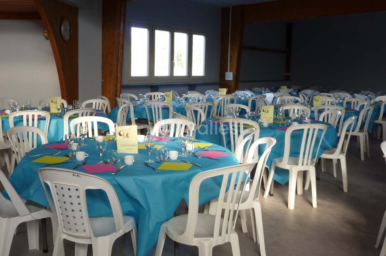 Salle décorée pour un événement, avec des tables rondes couvertes de nappes bleues et des chaises blanches.