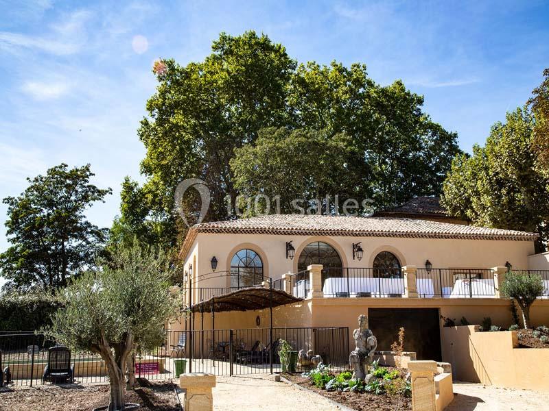 Façade d'une maison méditerranéenne entourée de végétation, avec terrasse et statue dans le jardin.