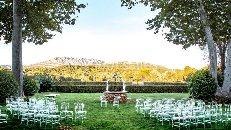 Chaises blanches disposées en extérieur devant une arche décorative, avec vue sur un paysage de montagne et de verdure.