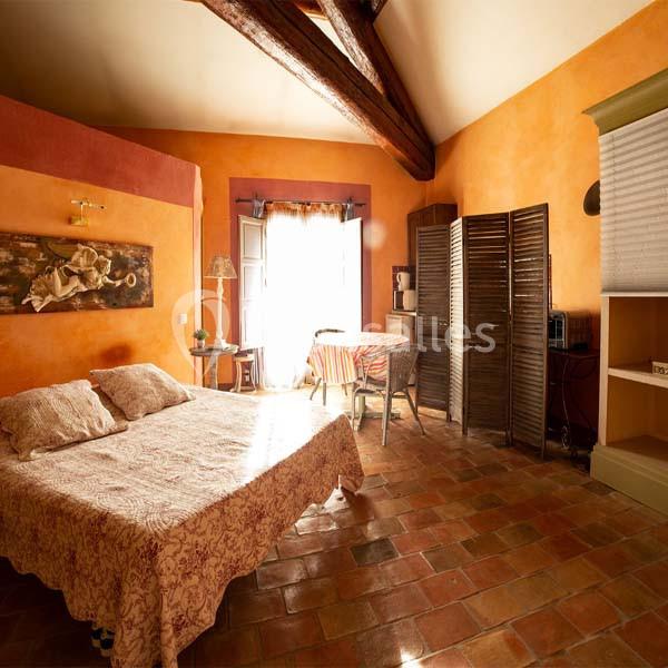Chambre lumineuse avec murs orange, lit double, sol en terre cuite, table près d'une fenêtre et cloison en bois.