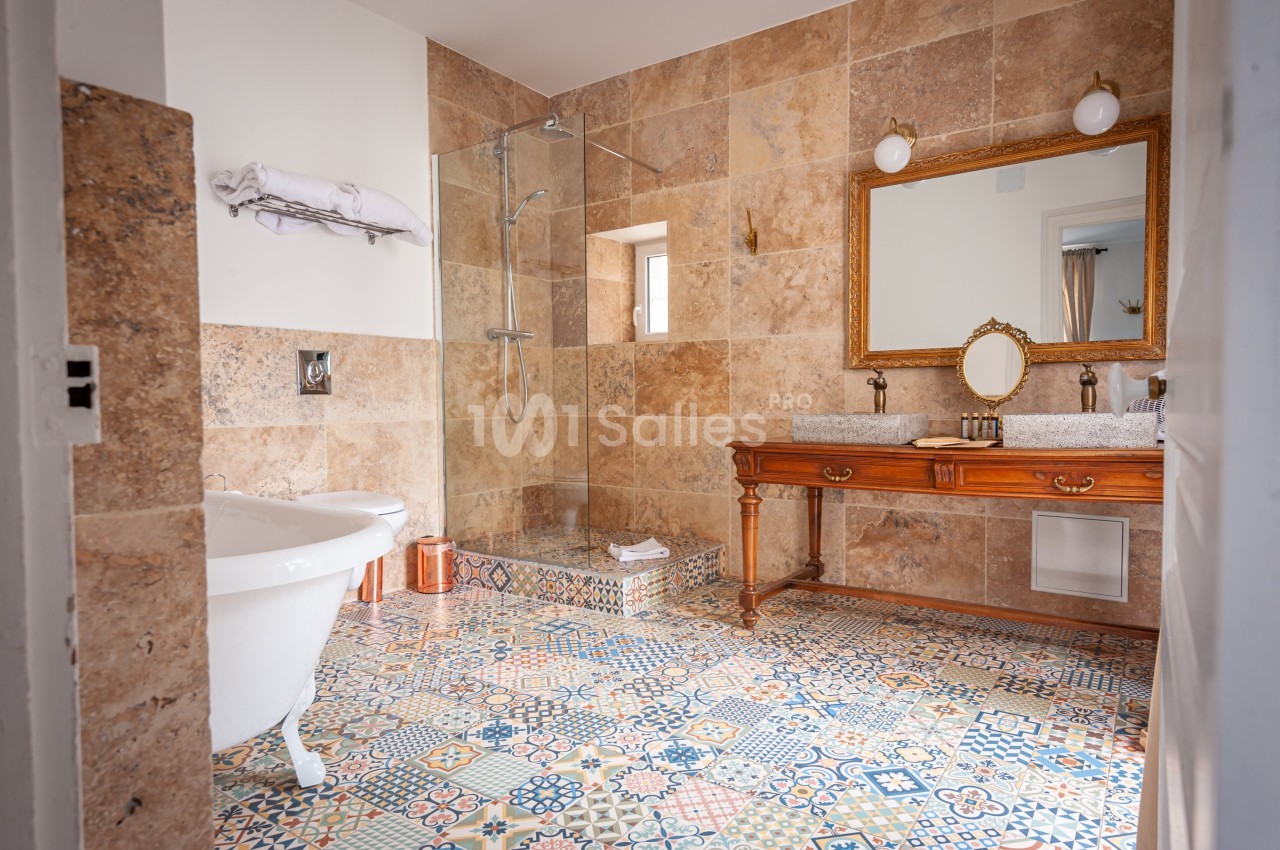 Salle de bain avec baignoire sur pieds, douche à l'italienne, carrelage coloré et meuble en bois avec miroir.