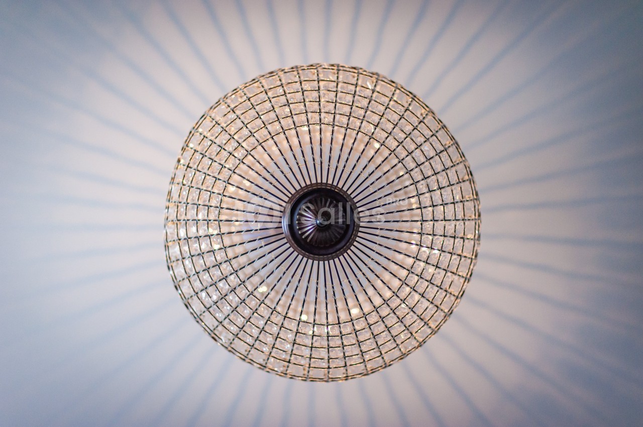 Vue en contre-plongée d'un lustre circulaire en verre avec des motifs rayonnants projetés sur le plafond.