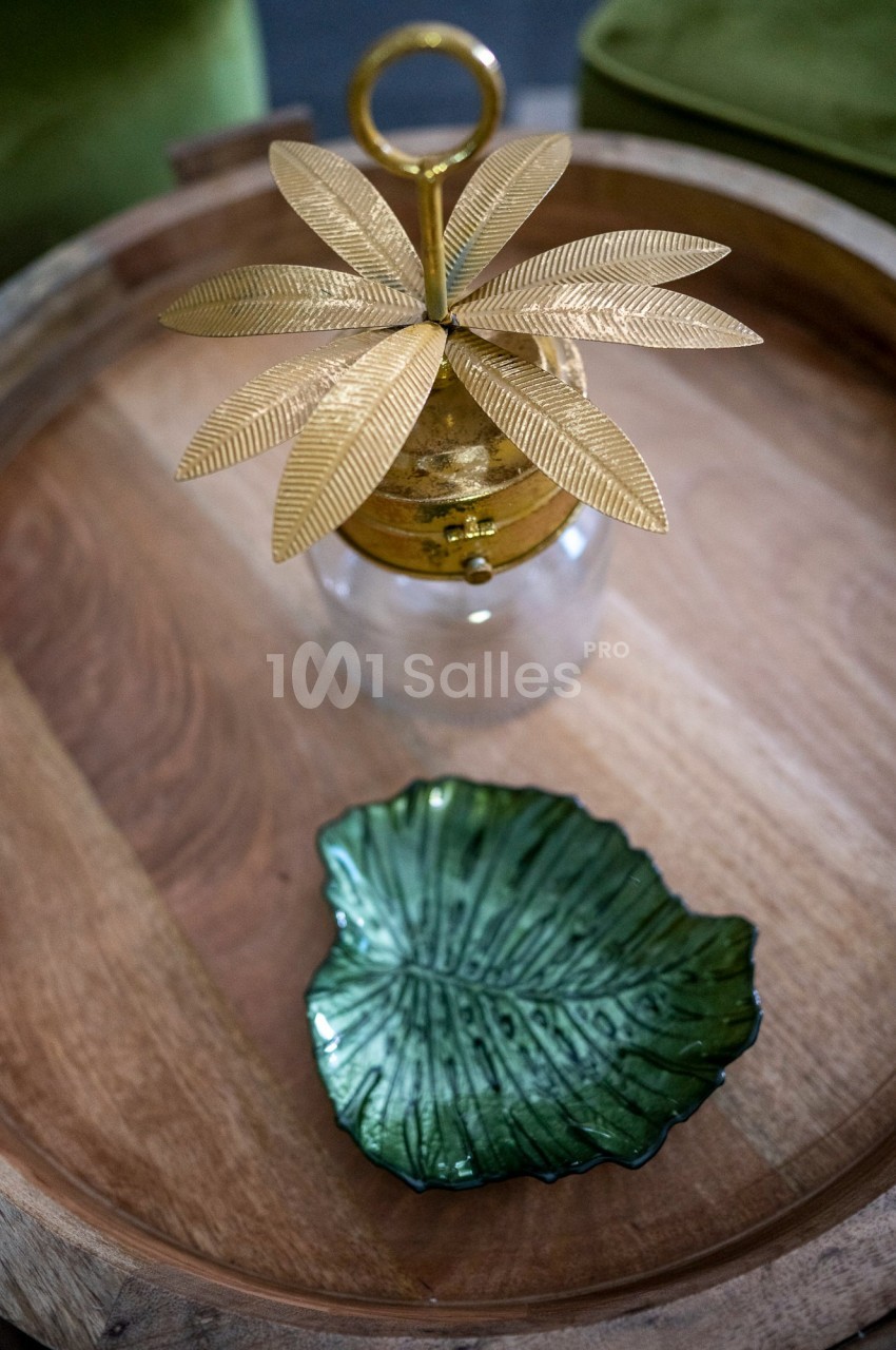 Objet décoratif doré en forme de feuilles et petite assiette verte en céramique sur un plateau en bois.