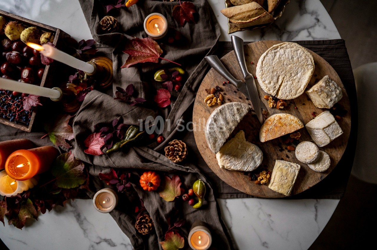 Plateau de fromages variés sur une table décorée avec des bougies, des feuilles d'automne et des fruits secs.