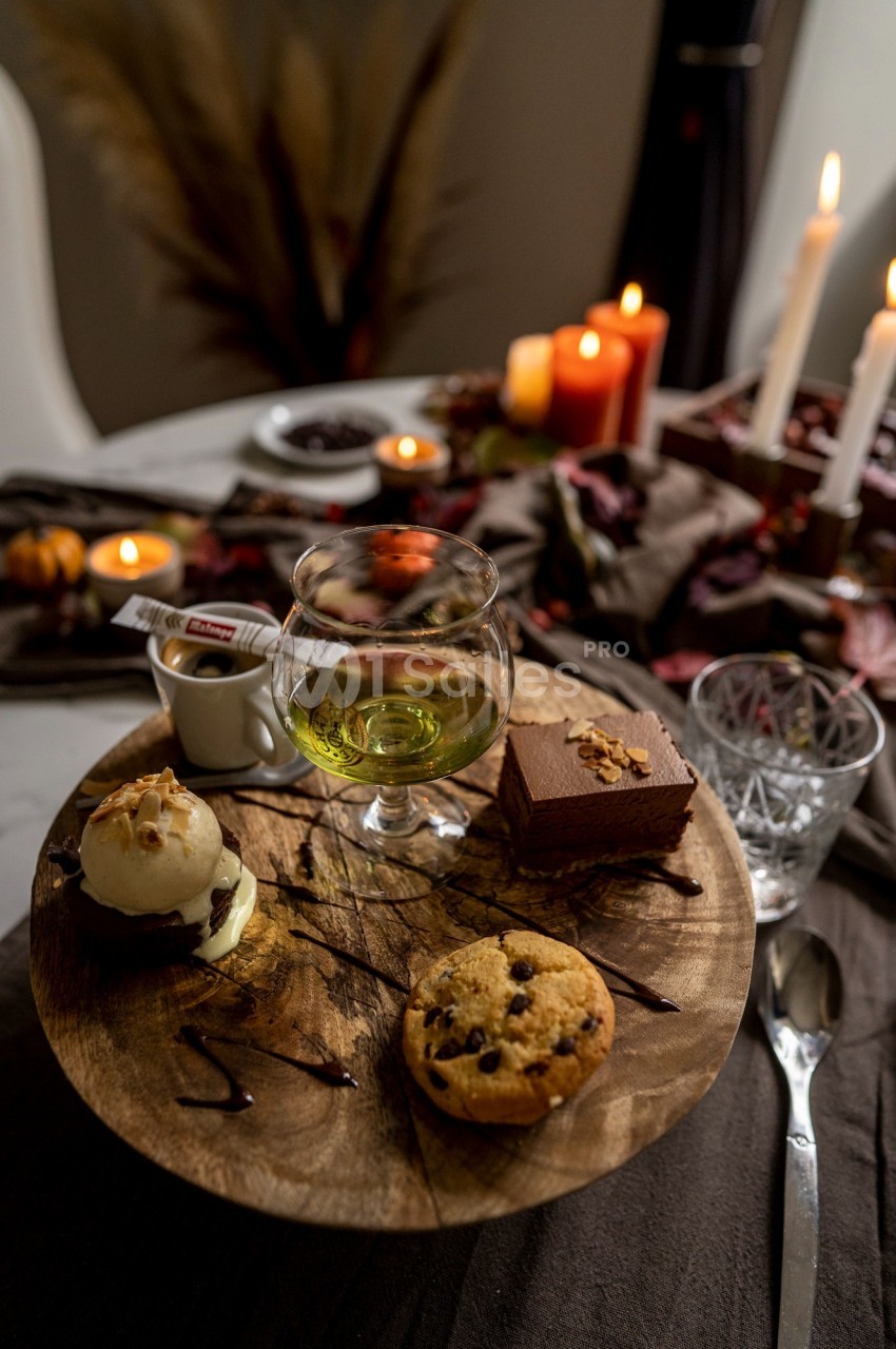 Dessert sur une planche en bois avec glace, muffin, gâteau au chocolat, verre de liqueur et bougies en arrière-plan.