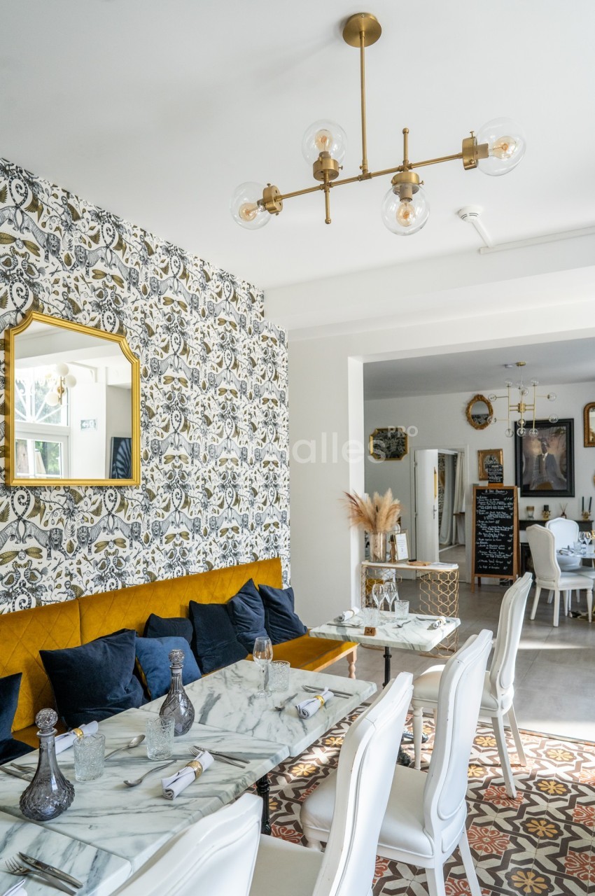 Salle à manger lumineuse avec tables en marbre, chaises blanches, banquette jaune et décoration murale élégante.