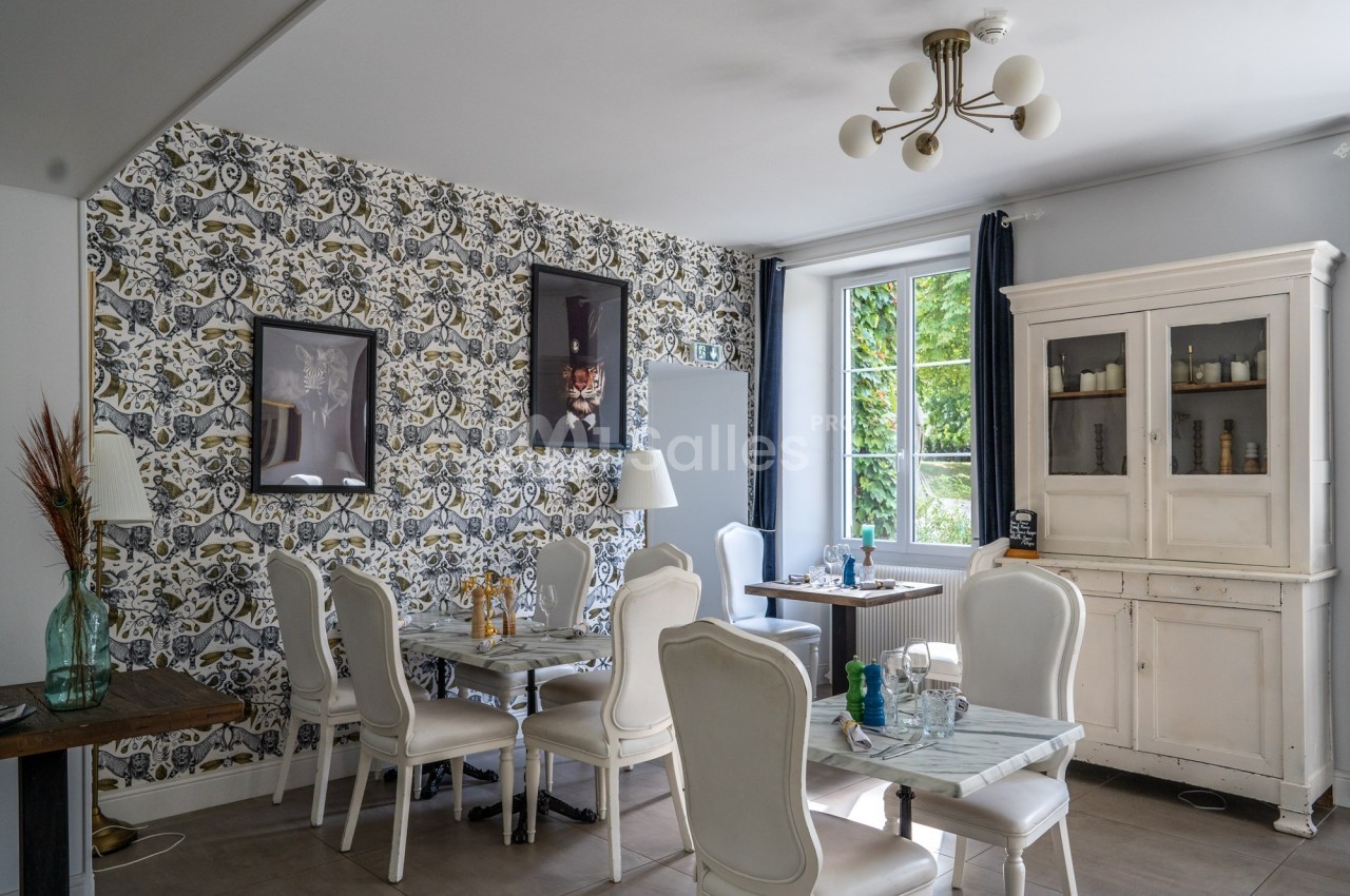 Salle à manger lumineuse avec des chaises blanches, des tables en marbre, un buffet ancien et un mur à motifs.