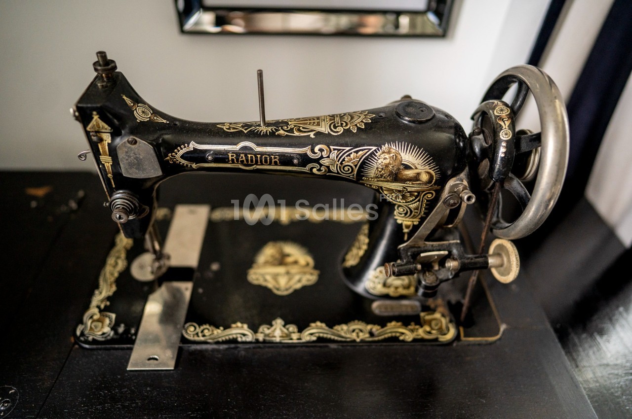 Machine à coudre ancienne noire avec des motifs dorés, posée sur une table en bois sombre.
