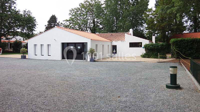 Bâtiment blanc moderne avec toit en tuiles rouges, entouré d'arbres et d'une cour en gravier.