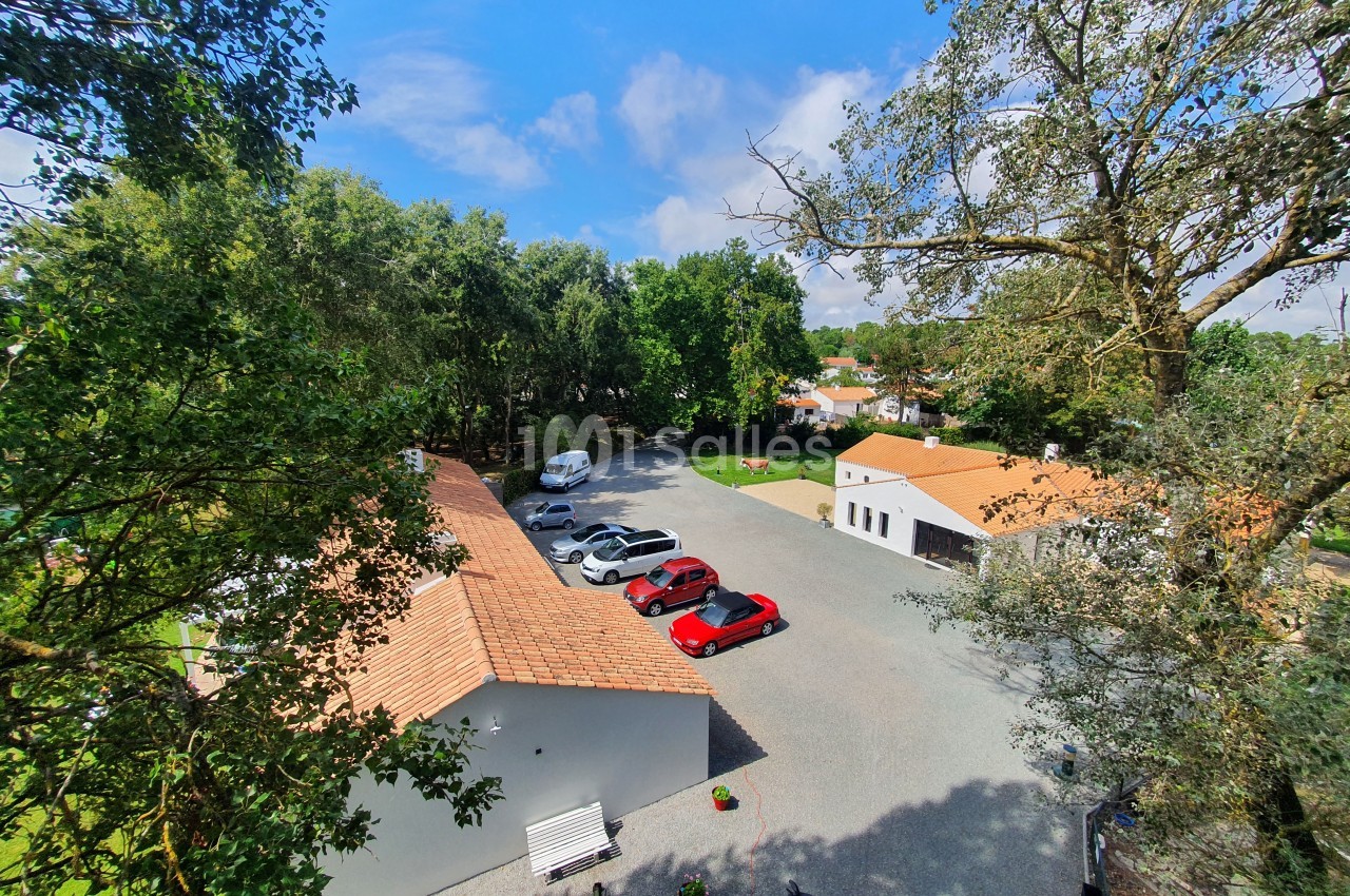 Vue aérienne d'une cour avec des bâtiments aux toits en tuiles, des voitures stationnées et des arbres environnants.