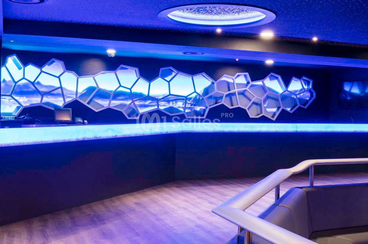 Comptoir lumineux avec éclairage bleu, décor mural en formes géométriques et plafond étoilé dans un espace moderne.
