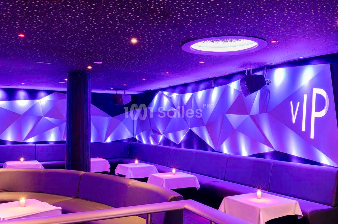 Salle de réception moderne avec éclairage violet, banquettes, tables basses et décorations géométriques lumineuses.