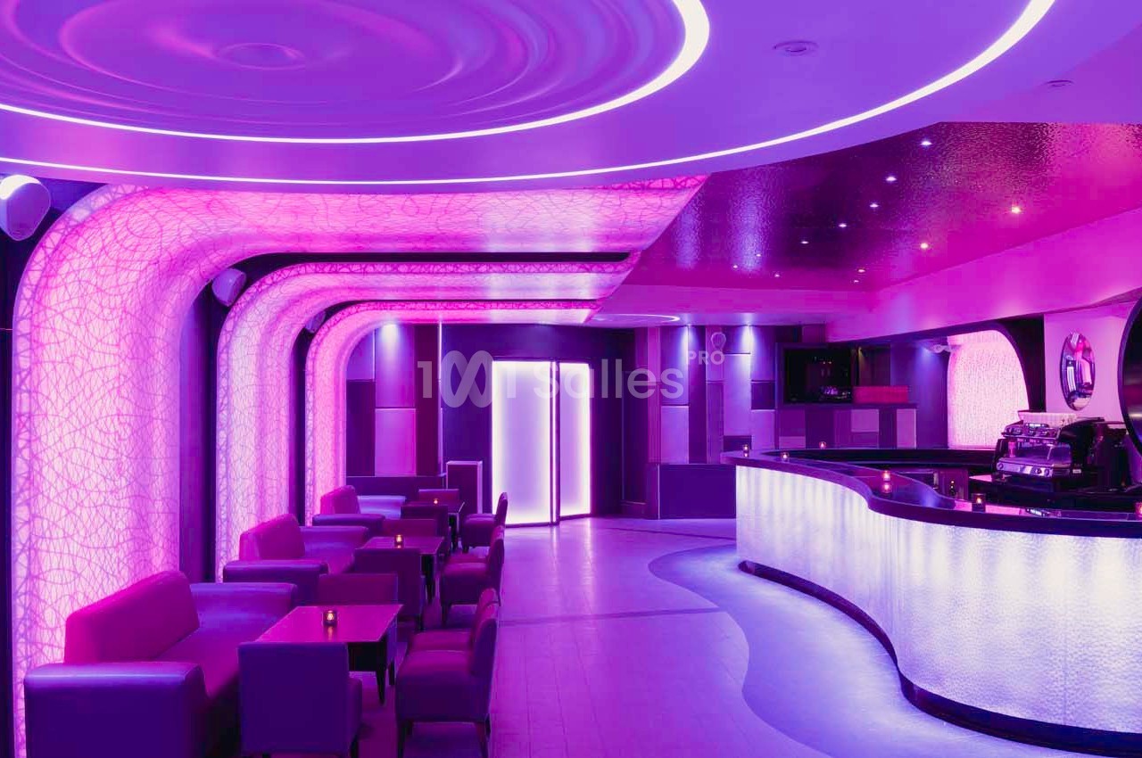 Intérieur d'un bar moderne avec éclairage violet, comptoir incurvé et sièges disposés dans un espace lumineux.