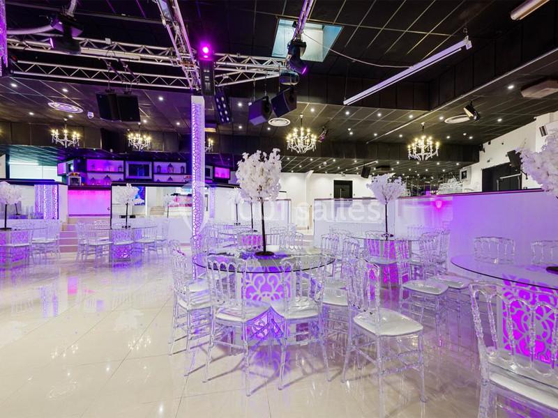 Salle de réception moderne avec tables et chaises transparentes, éclairage violet et lustres suspendus.