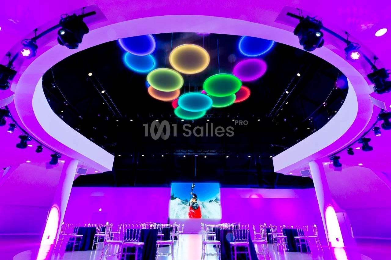 Salle moderne éclairée de lumières violettes, avec des tables et des chaises transparentes, et des cercles lumineux…