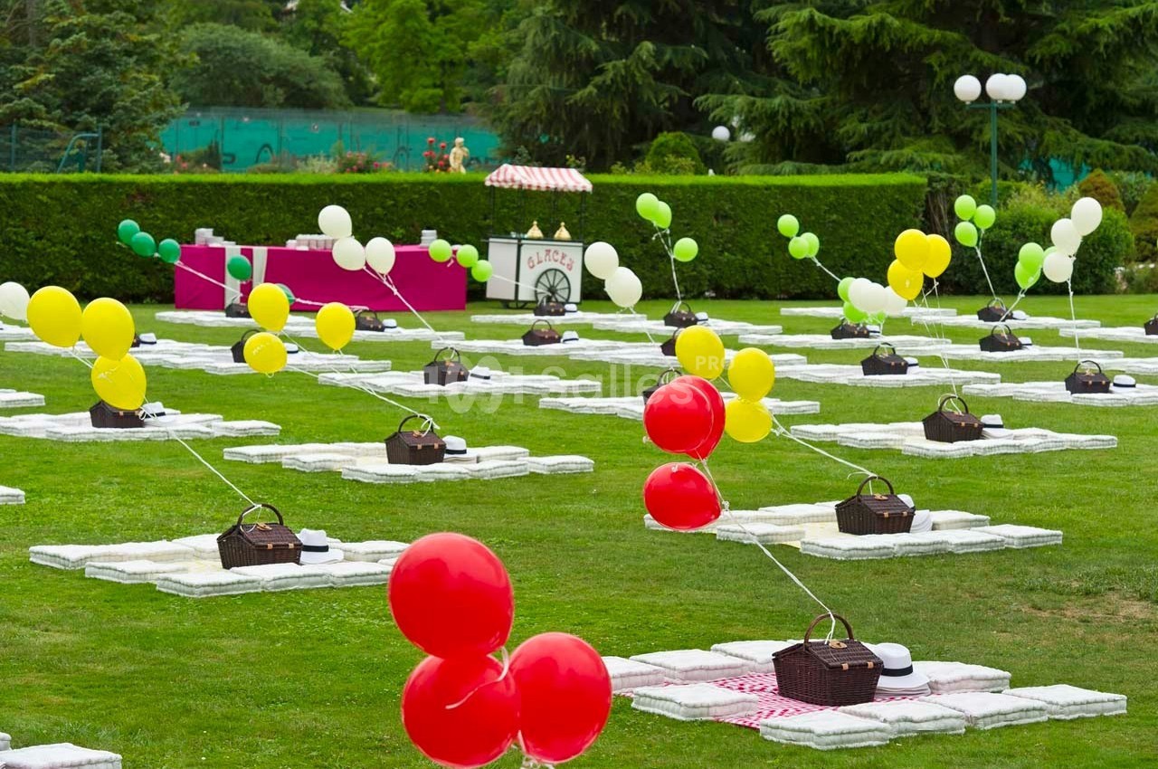 Des nappes blanches disposées sur une pelouse avec des paniers de pique-nique et des ballons colorés attachés.