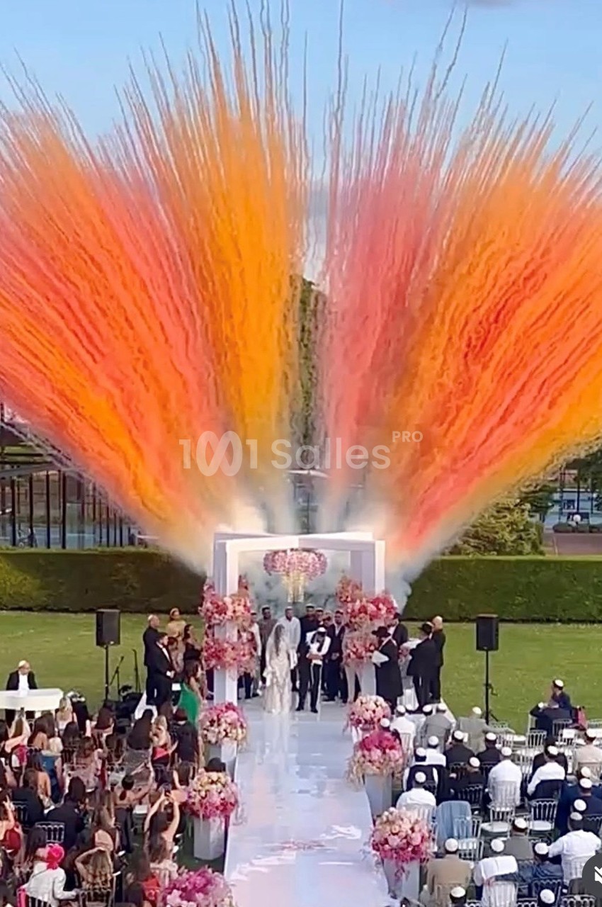 Cérémonie de mariage en plein air avec des jets de fumée colorée orange et jaune en arrière-plan.