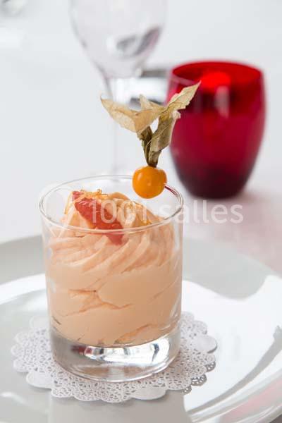 Verrine de mousse orange décorée d'un physalis et d'un segment d'agrume, servie sur une napperon blanc.