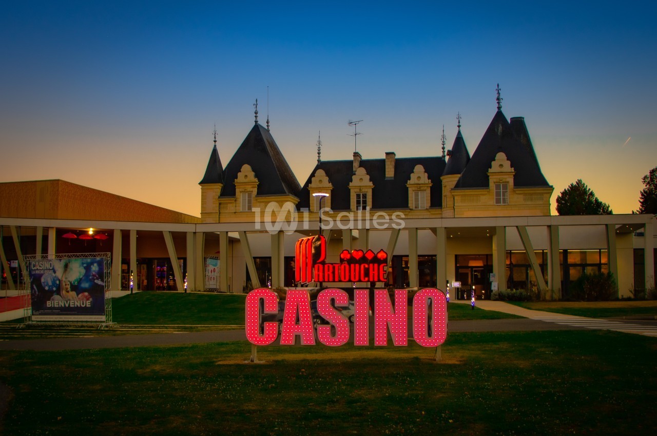 Façade d'un casino avec enseigne lumineuse rouge et bâtiment de style château en arrière-plan, au crépuscule.
