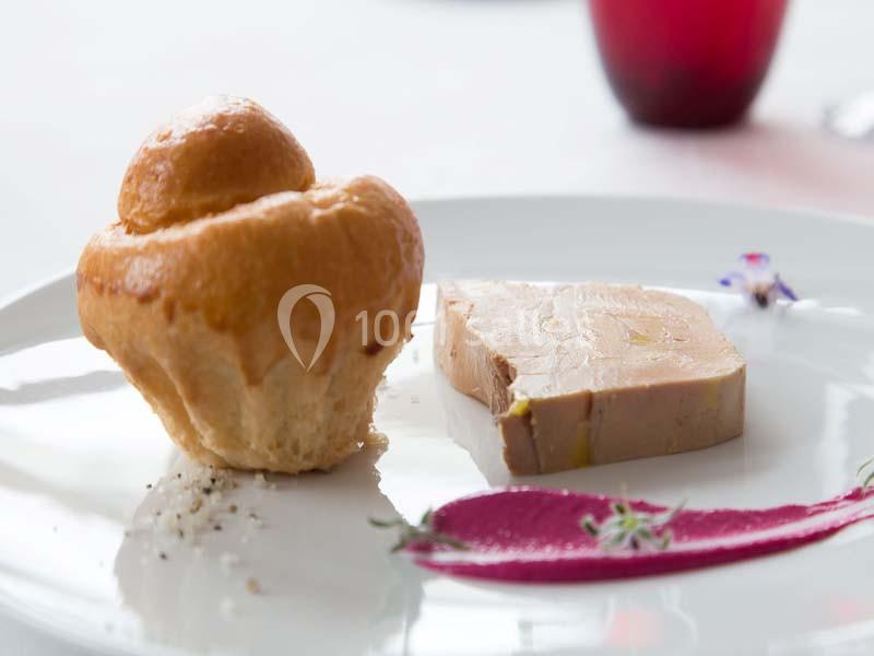 Brioche dorée et tranche de foie gras accompagnées d'une purée violette décorée de fleurs sur une assiette blanche.