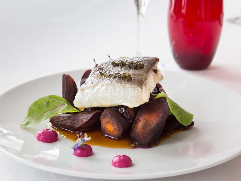 Filet de poisson sur un lit de carottes violettes, sauce et garniture de feuilles vertes, présenté sur une assiette blanche.