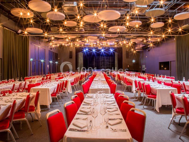 Salle de réception avec tables dressées, chaises rouges et éclairage suspendu créant une ambiance chaleureuse.
