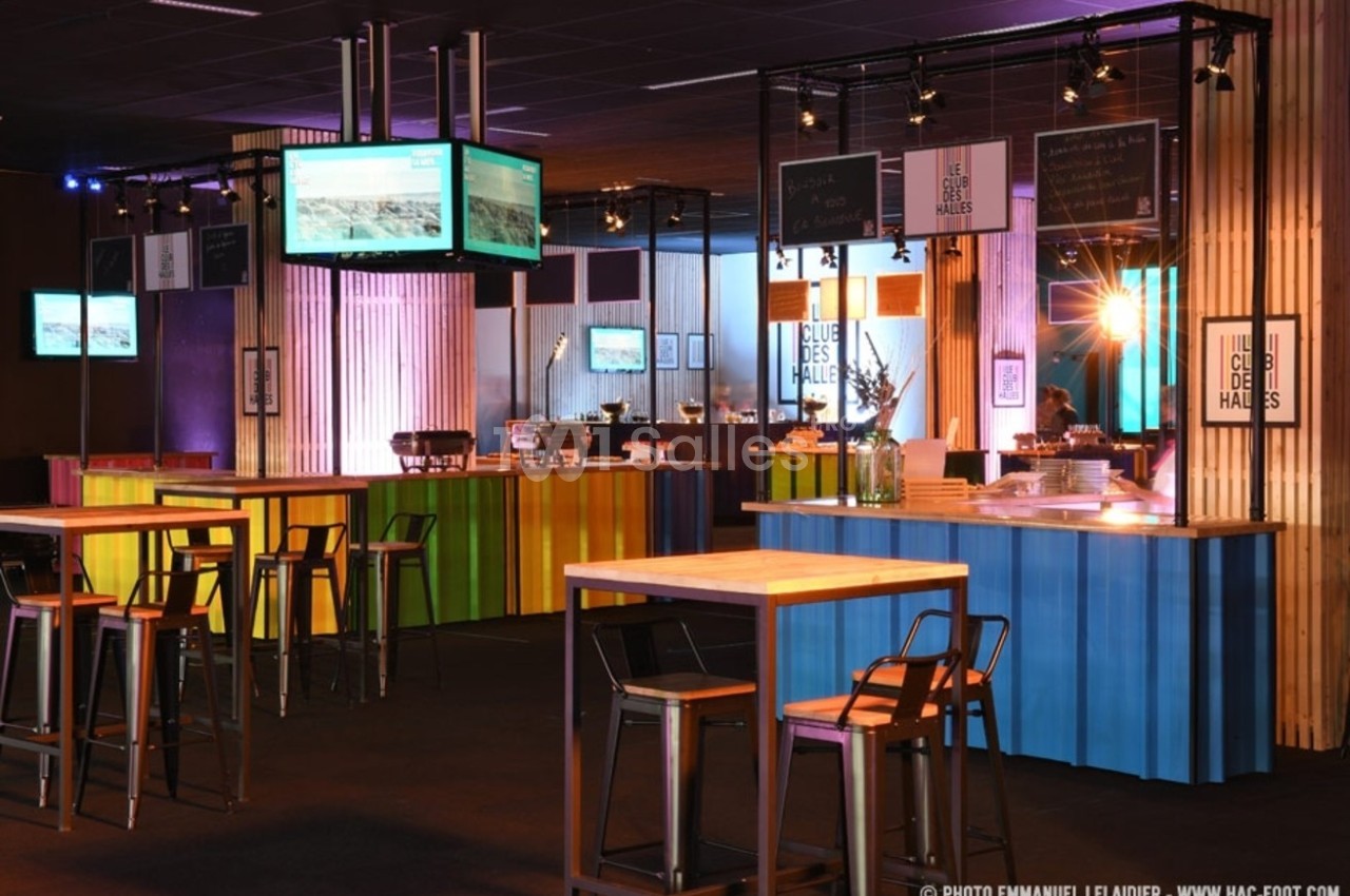 Salle aménagée avec des tables hautes et des comptoirs colorés, éclairée par des lumières chaleureuses.