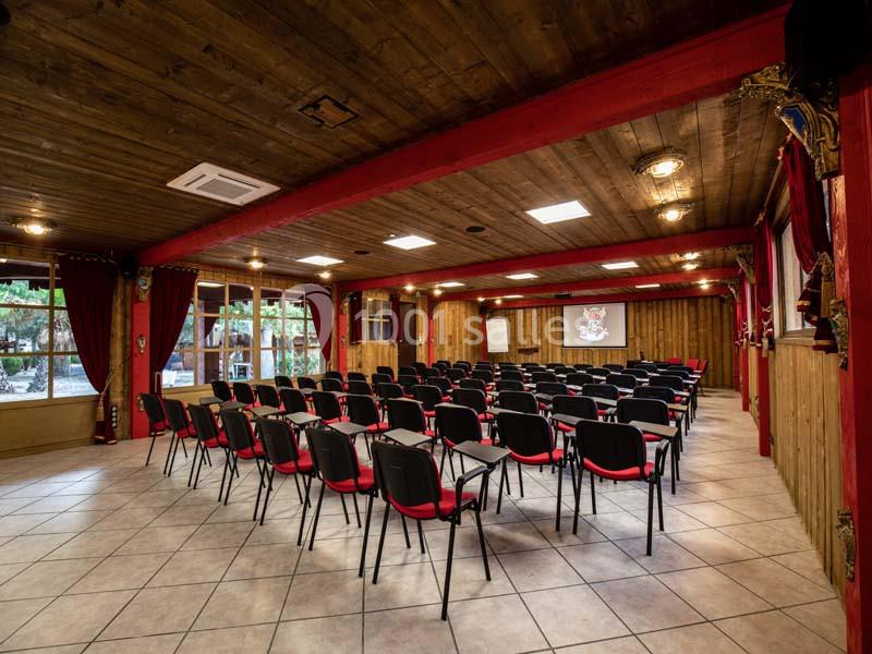 Salle de conférence avec rangées de chaises noires et rouges, écran de projection et décor en bois.