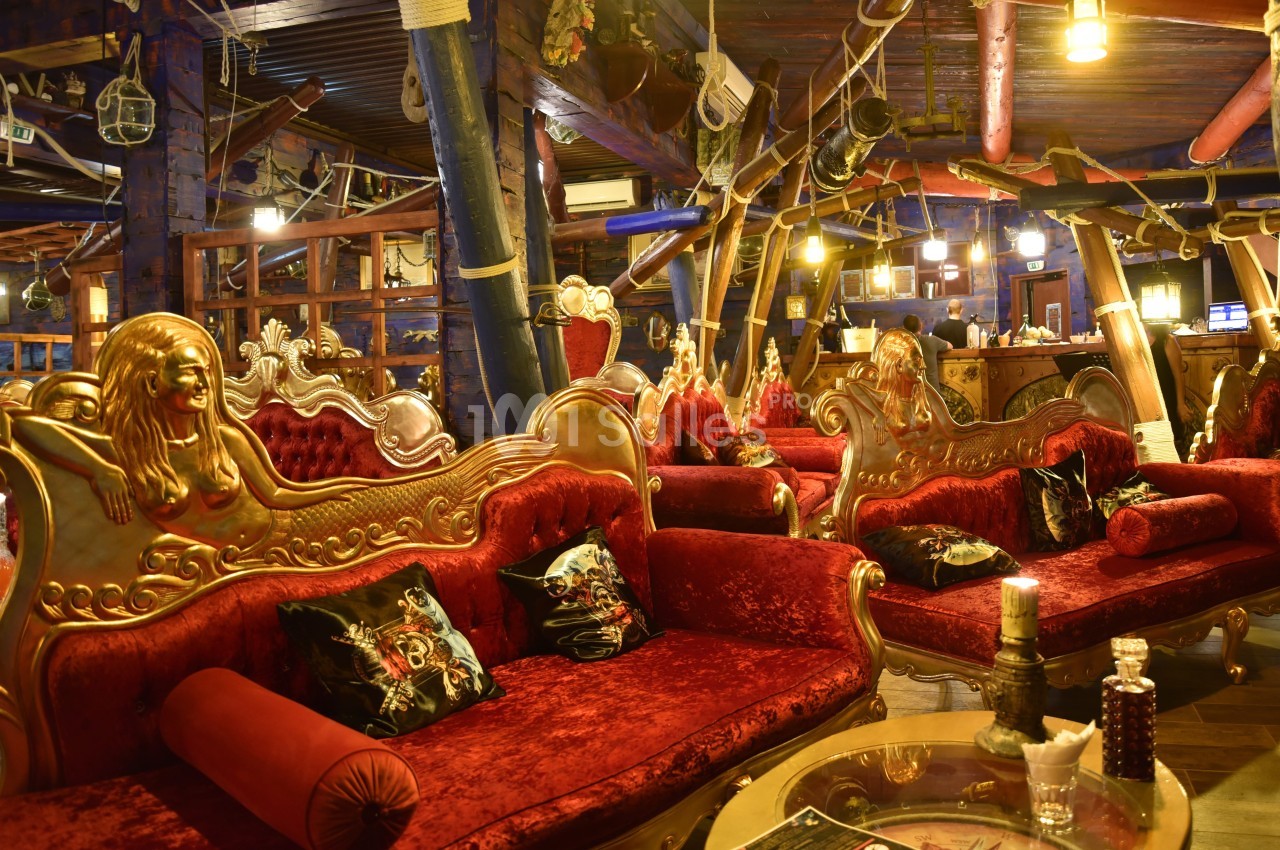 Salon décoré de façon éclectique avec des canapés rouges ornés de sculptures dorées et un éclairage chaleureux.