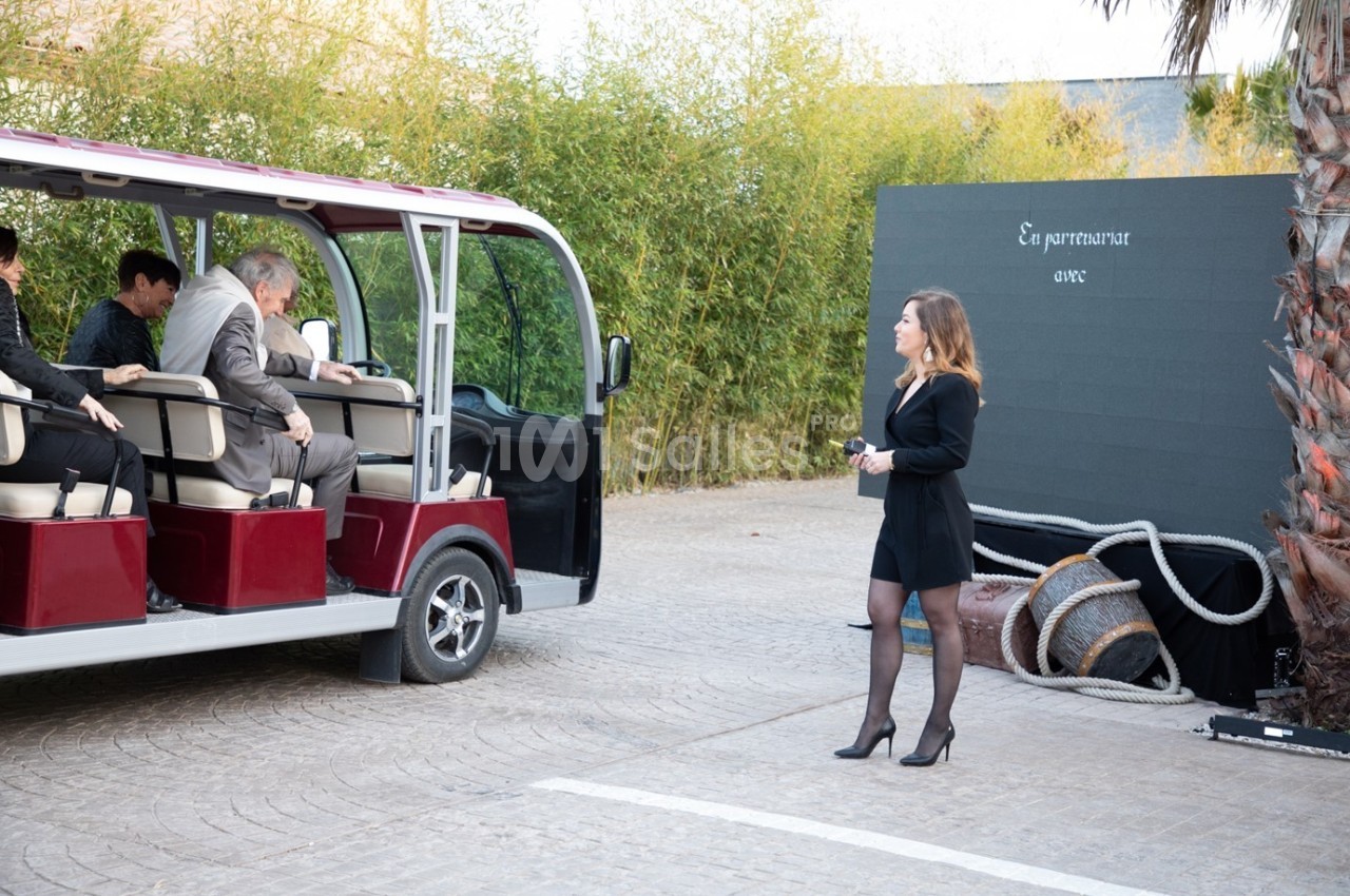 Une femme en tenue professionnelle se tient près d'une navette électrique où des passagers montent.