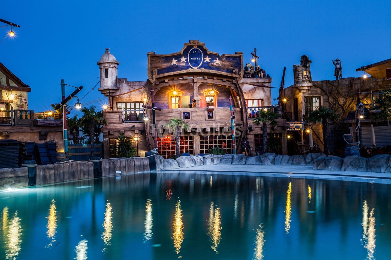 Façade d'un bâtiment à thème pirate éclairé la nuit, avec une piscine calme au premier plan.