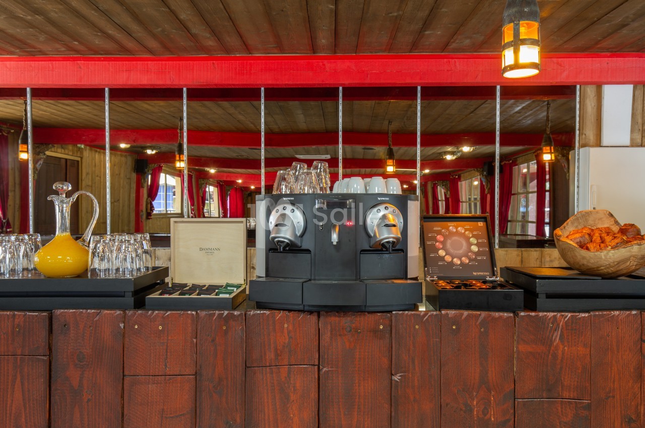 Machine à café avec tasses, carafe, viennoiseries et présentoirs dans un décor en bois avec éclairage chaleureux.