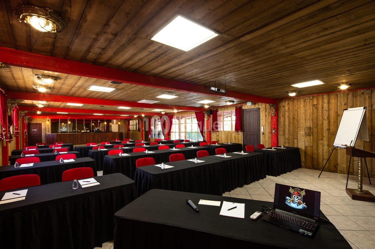 Salle de conférence avec des tables couvertes de nappes noires, chaises rouges, un projecteur et un tableau de présentation.