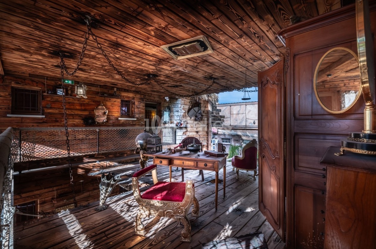 Bureau en bois rustique avec chaise rouge, objets anciens et décorations suspendues dans un espace intérieur chaleureux.