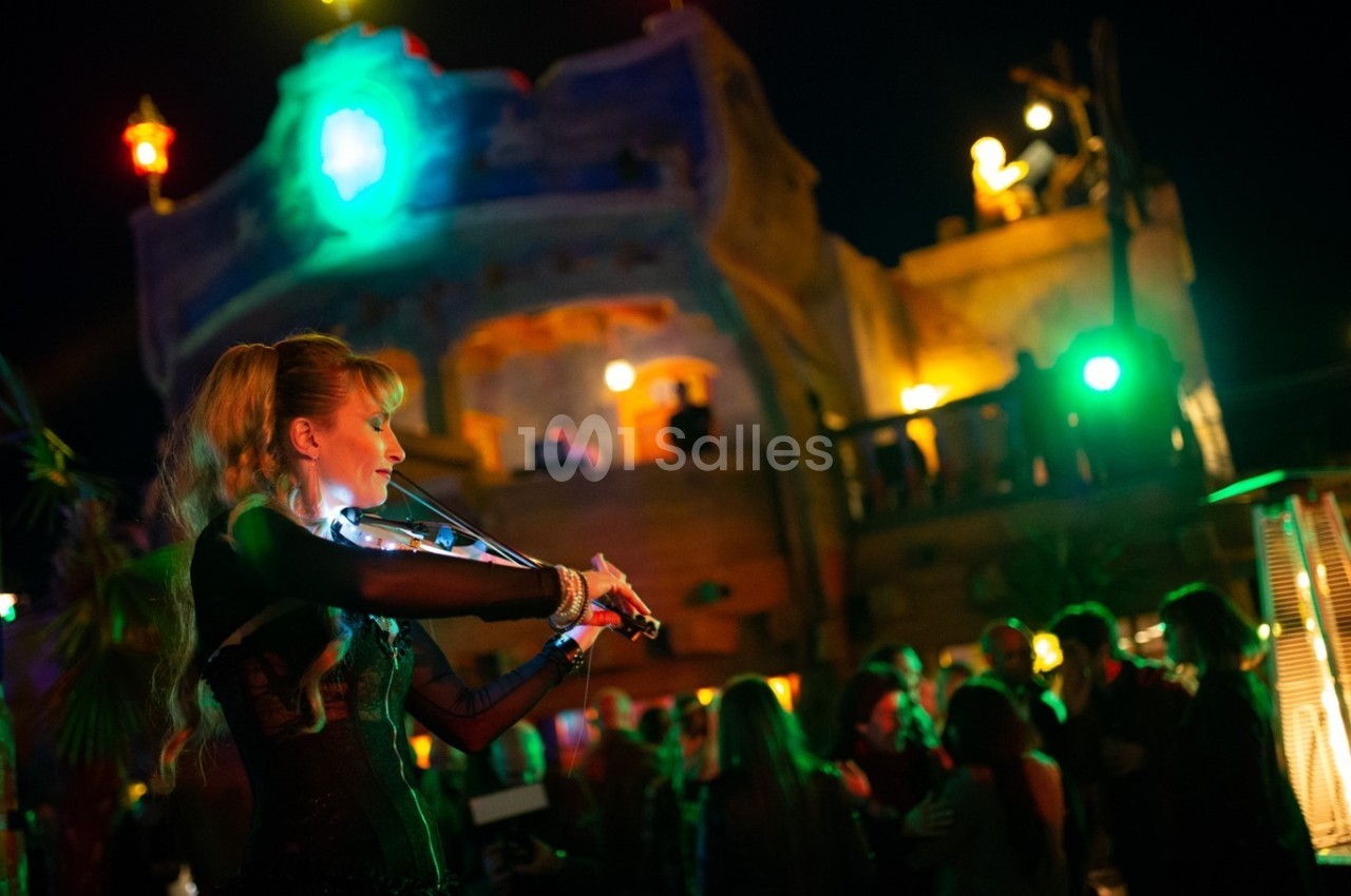 Une violoniste joue devant un bâtiment illuminé, entourée d'une foule dans une ambiance nocturne festive.