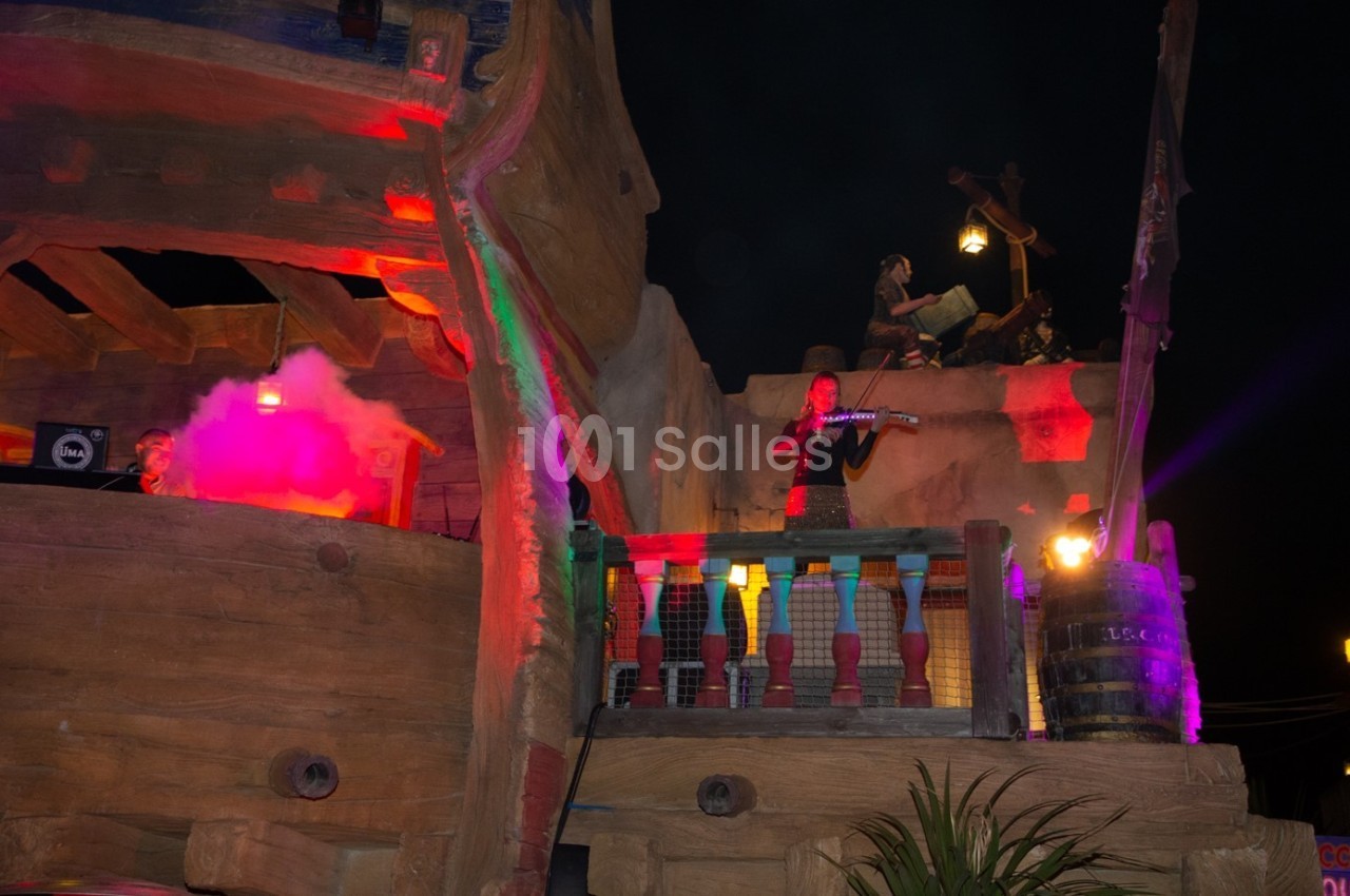 Un musicien joue du violon sur une structure en bois éclairée par des lumières colorées, de nuit.