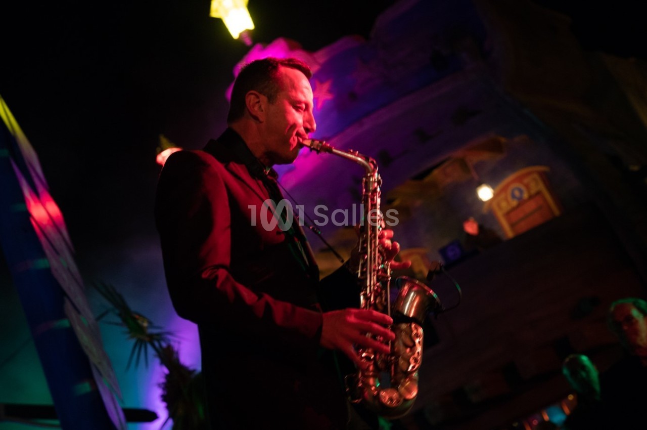 Un musicien joue du saxophone sous des lumières colorées dans une ambiance nocturne.