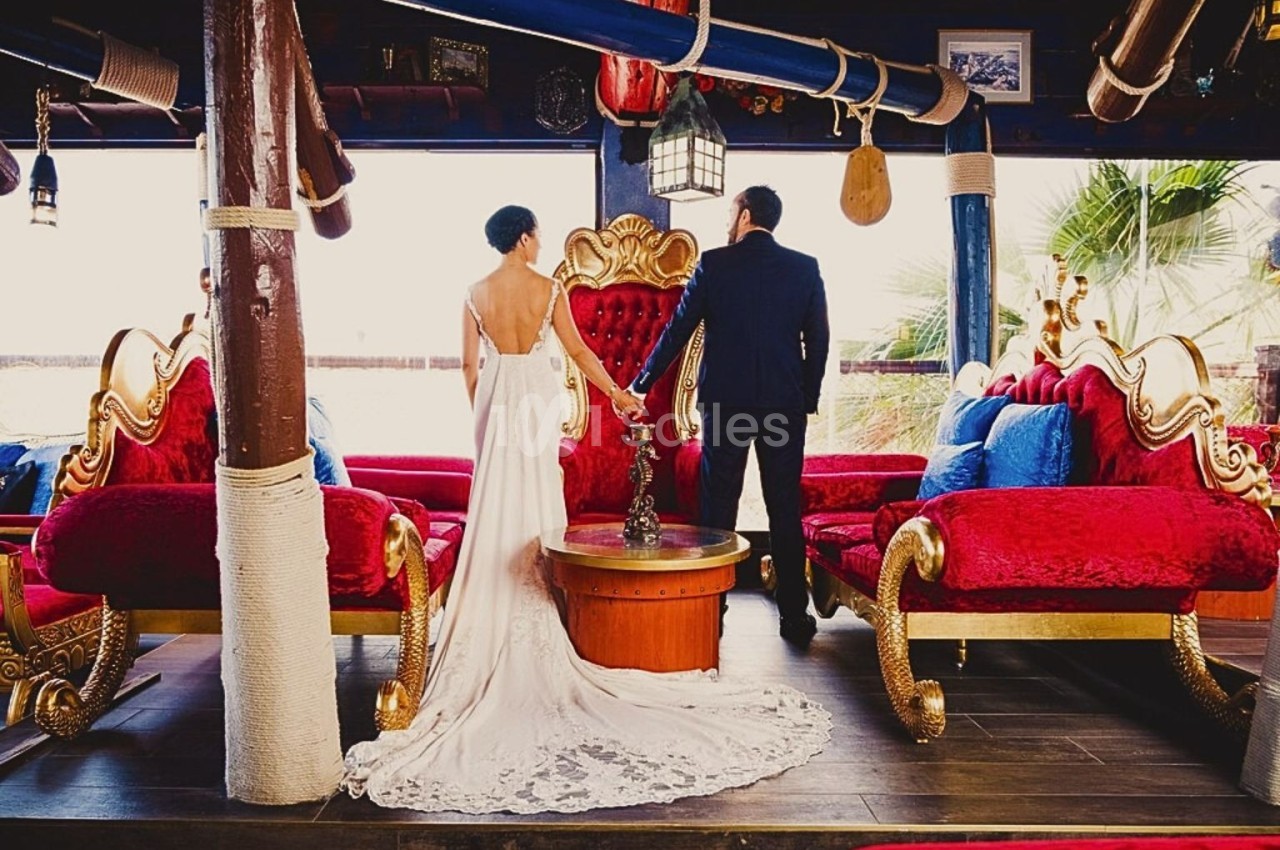 Un couple en tenue de mariage se tient debout dans un salon décoré de fauteuils rouges et dorés.