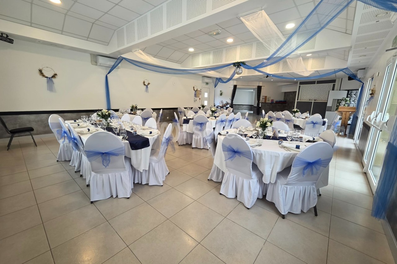 Salle de réception décorée en bleu et blanc avec tables dressées et chaises ornées de nœuds bleus.