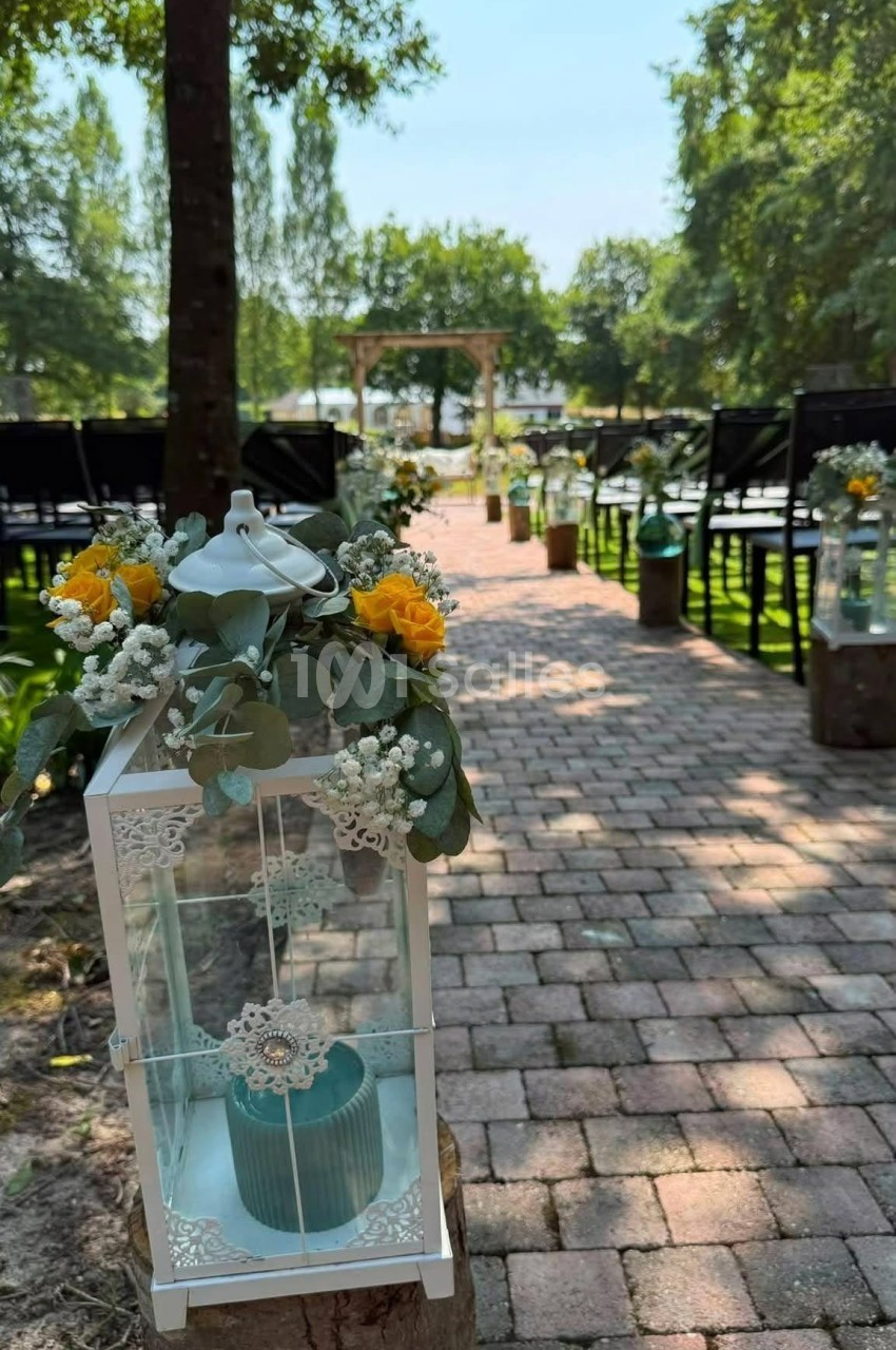 Allée extérieure pavée décorée pour une cérémonie, avec lanternes blanches ornées de fleurs jaunes et blanches.